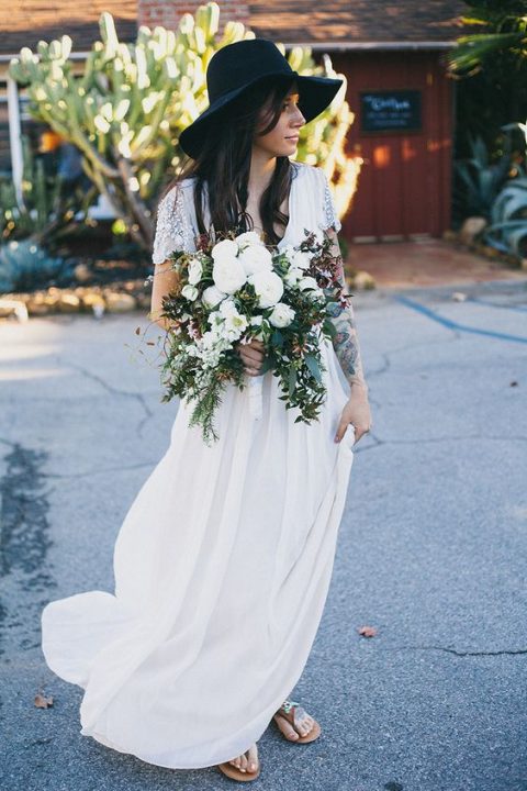 a boho bride showing off her tattoos and wearing a black hat that contrasts her dress a lot