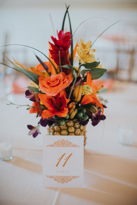 a pineapple wedding centerpiece wih orange, red and yellow blooms and some greenery