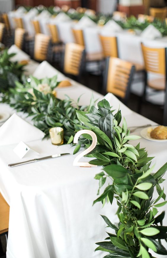 a lush and textural greenery table runner with small candles in candle holders is a cute idea