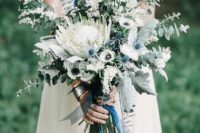 22 a pale and delicate wedding bouquet with blue thistles, a king protea, white anemones and herbs and eucalyptus