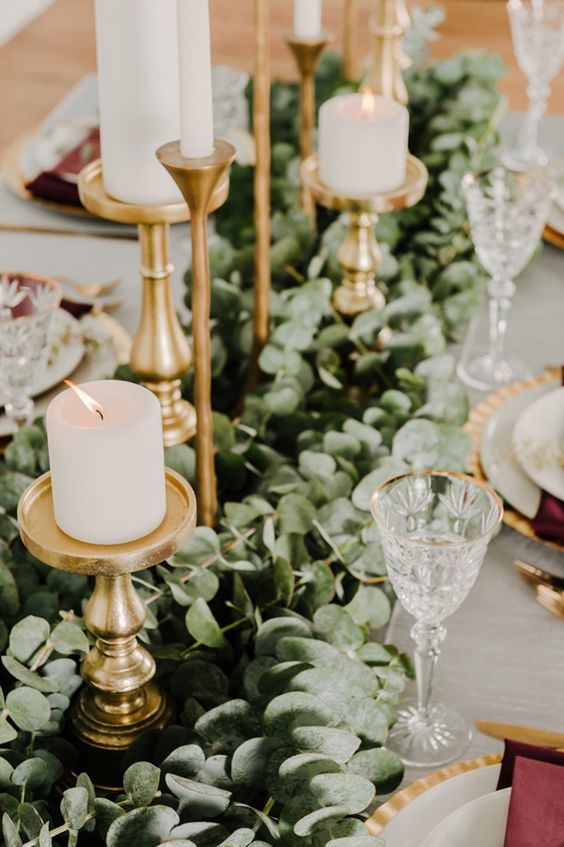 a lush eucalyptus table runner with gold candle holders and pillar candles for a timelessly elegant look