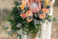 23 a textural cascading wedding bouquet with a king protea, peachy and yellow blooms, blue thistles and ferns and eucalyptus