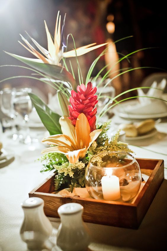 a tropical beach centerpiece with a box of sand, a candle and some tropical blooms