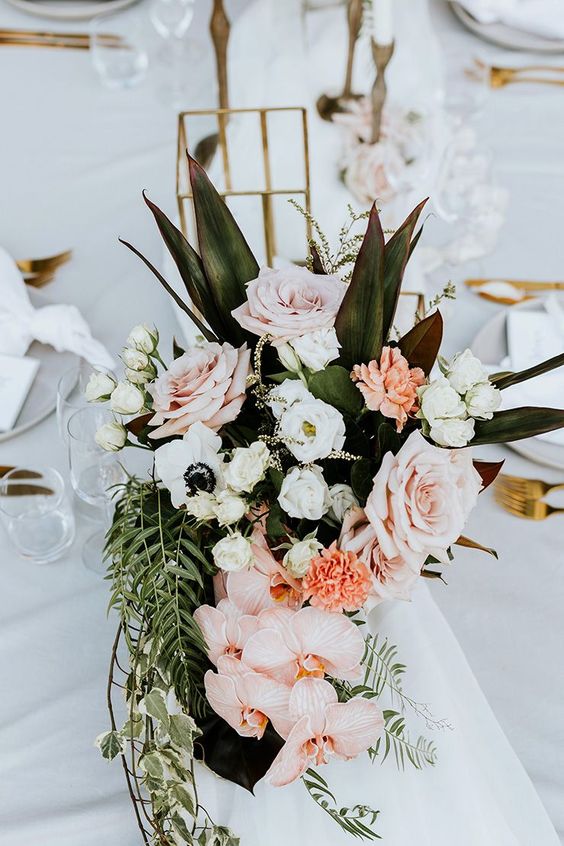 a tropical wedding centerpiece of roses, anemones, orchids and greenery and leaves