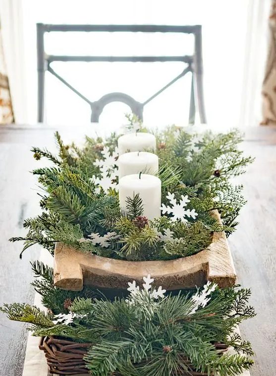 a beautiful winter wedding centerpiece of a basket with evergreens and a breadbowl with evergreens and candles plus pinecones and snowflakes