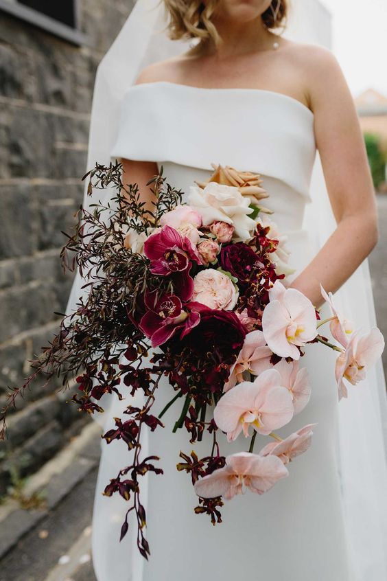 a bold cascading wedding bouquet of purple poenies and orchids, blush orchids and greenery and neutral roses