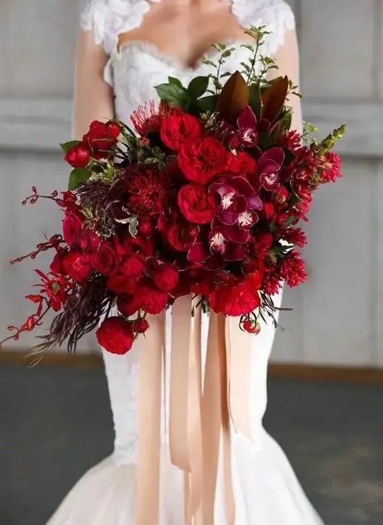 a breathtaking jewel tone wedding bouquet with deep red, burgundy and purple blooms, foliage and greenery and long ribbon