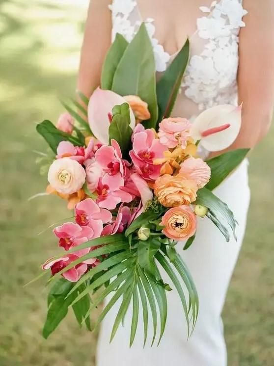 a bright tropical wedding bouquet of pink orchids, yellow ranunculus, neutral anthurium, greenery and fronds