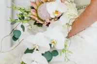 a cascading tropical wedding bouquet with white orchids, greenery and a king protea for a bold statement