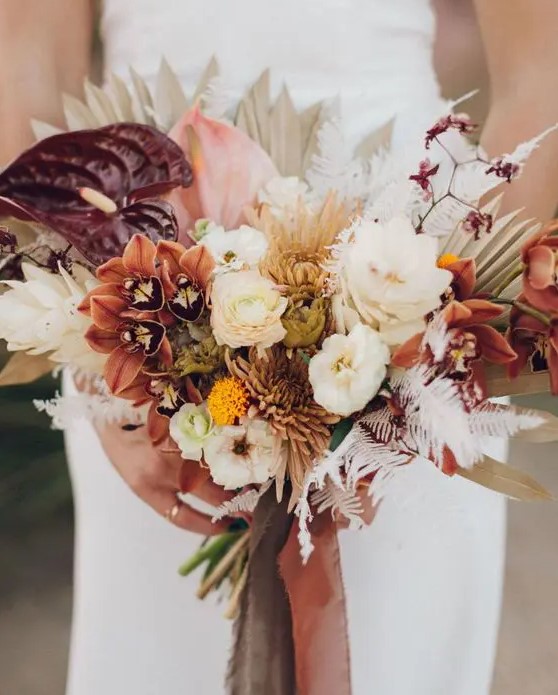a catchy fall wedding bouquet of white and rust blooms, burgundy anthurium and liles, dried fronds and leaves