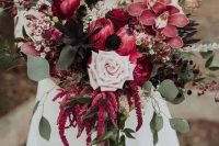a catchy wedding bouquet of king proteas, orchids, a pale blush rose, dried bloom branches, amaranthus and greenery for the fall