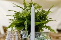 a cluster wedding centerpiece of potted fern, a candle, some candleholders and a terrarium with greenery
