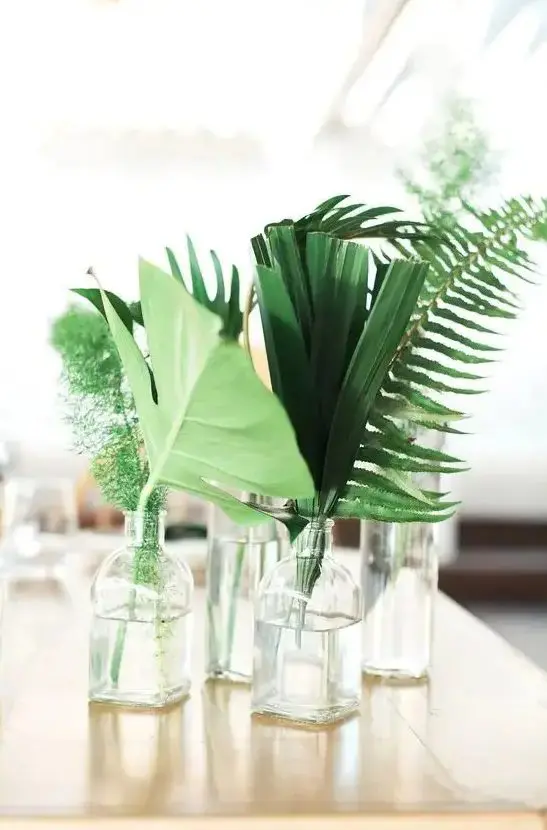 a cluster wedding centerpiece of vases and bottles, tropical leaves, greenery and fern is a lovely idea for a tropical wedding