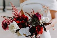 a contrasting wedding bouquet of burgundy orses and peonies, white roses and orchids and bold leaves is a cool idea