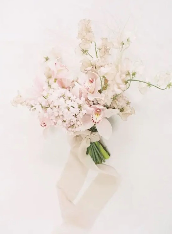 a delicate blush and white wedding bouquet with orchids and sweet peas, with neutral ribbons and beads for a spring bride