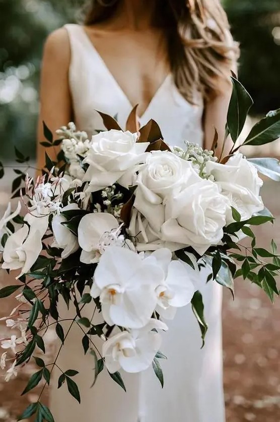 a dimensional white wedding bouquet with roses, orchids and other blooms plus greenery and magnolia leaves