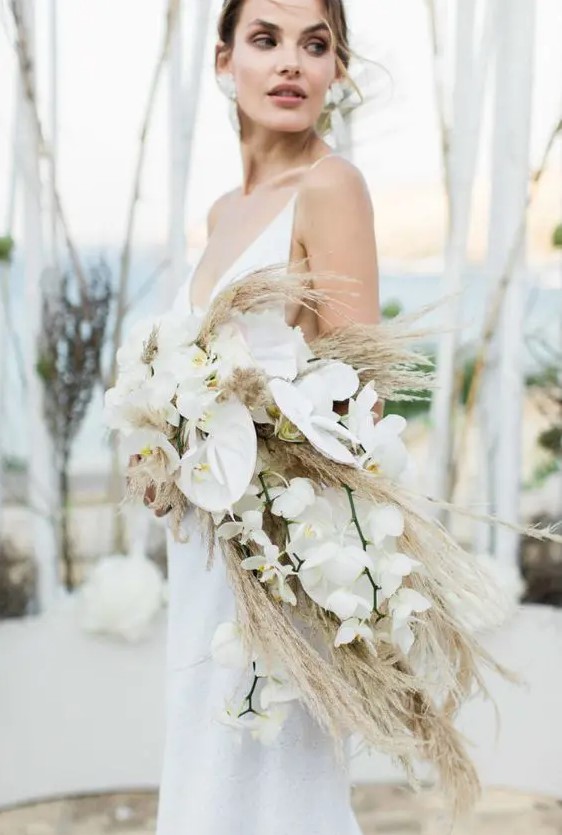 a dreamy cascading boho wedding bouquet of white orchids and pampas grass is a cool idea for a modenr boho bride