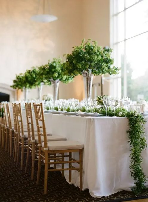 a lush greenery table runner and tall matching centerpieces make the tablescape look very fresh and very spring-like