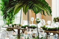 a lush tropical wedding centerpiece of tropical leaves on a tall black metal stand and a matching decoration on the table
