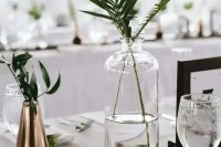 a modern clsuter wedding centerpiece of a clear and copper vase with greenery and a black and white table number for a modern wedding