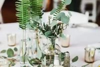 a modern cluster wedding centerpiece of vases and bottles with various greenery and candles is wow