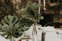 a modern tropical wedding centerpiece of large fronds and greenery, candles, beautiful mercury glass candleholders is chic