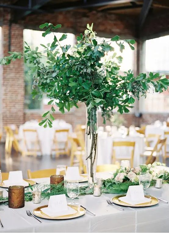 a natural greenery wedding centerpiece in a tall vase and a matching greenery runner