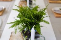 a pretty and easy wedding centerpiece of fern leaves, some potted greenery and a candle in a candlholder for a modern woodland wedding