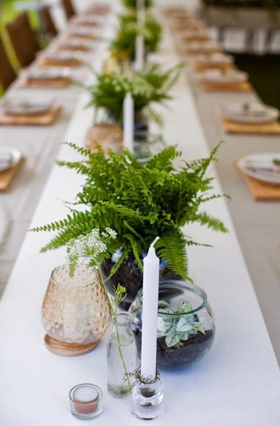 a pretty and easy wedding centerpiece of fern leaves, some potted greenery and a candle in a candlholder for a modern woodland wedding