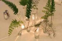 a relaxed cluster wedding centerpiece of matching glasses and various types of greenery and fern is amazing
