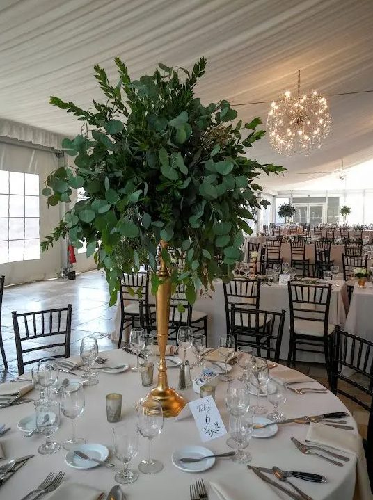 a tall foliage centerpiece with myrtle, seeded and silver dollar eucalyptus in a brass vase