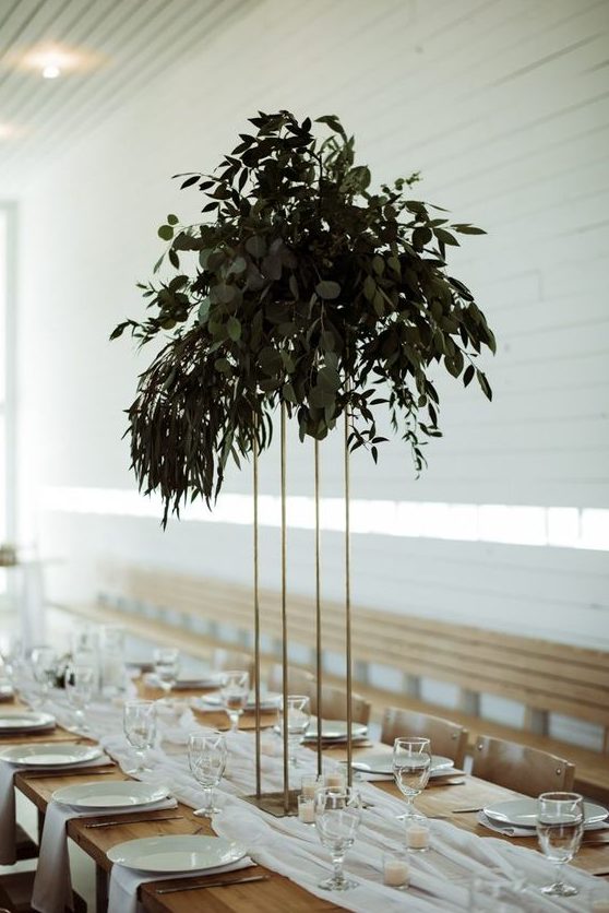 a tall minimalist wedding centerpiece on a gilded stand and with lush textural greenery won't take much table space