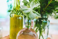 a woodland wedding centerpiece of a tree slice, bottles and vases, greenery, peachy blooms and a succulent is a very fresh and pretty idea