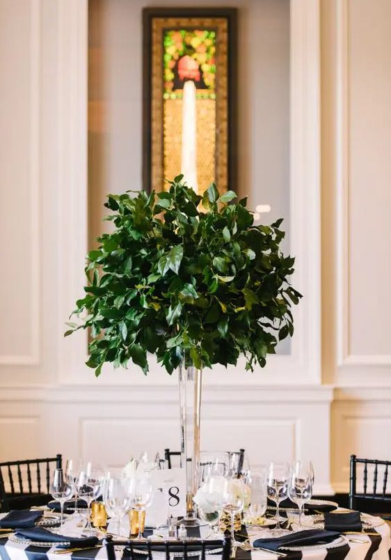 An ultra modern tall centerpiece of a clear vase and foliage looks amazing and follows the non floral wedding trend