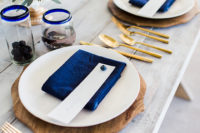 02 The wedding table setting was done with a whitewashed table, wooden chargers, navy napkins, sheer glasses with a blue rim and gold cutlery
