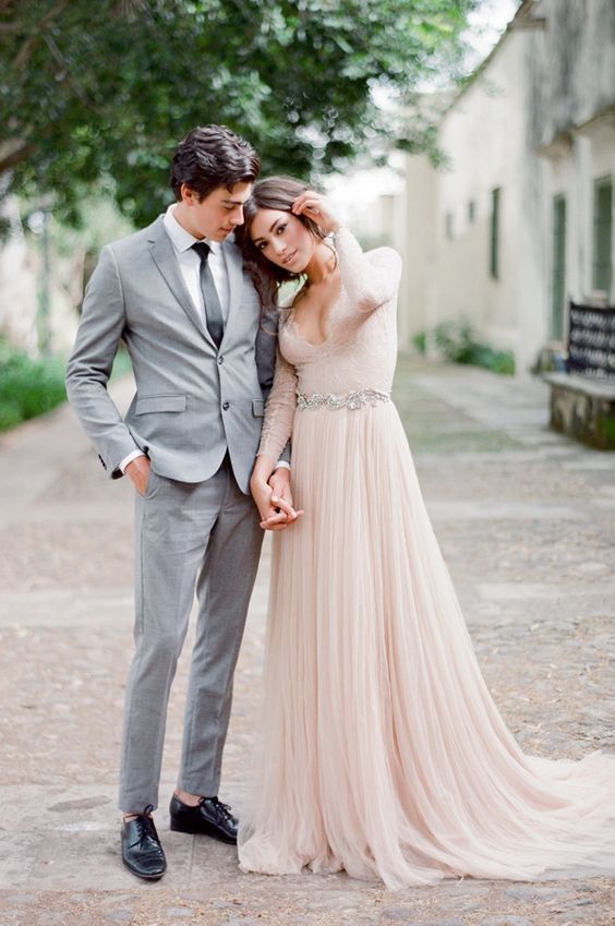 a blush wedding dress with a plunging neckline, long lace sleeves and an embellished sash
