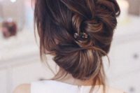 a braided low updo with a volume and some locks plus a rhinestone hairpiece