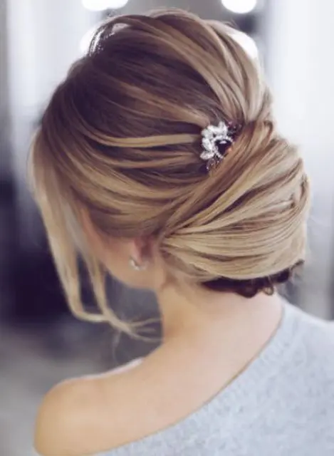 a textural low chignon hairstyle with a bump, bangs and a rhinestone hairpiece for an accent