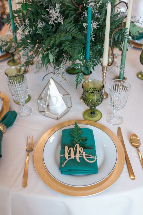 a fresh and bold table setting with greenery, a napkin and colored glasses plus gold touches