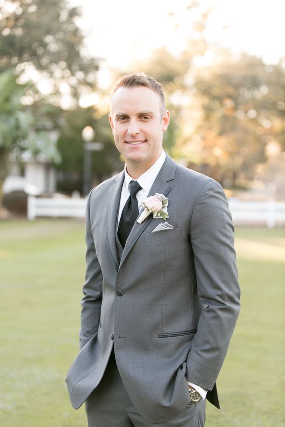 a grey three-piece groom's suit with a black tie and a floral boutonniere for a classic feel