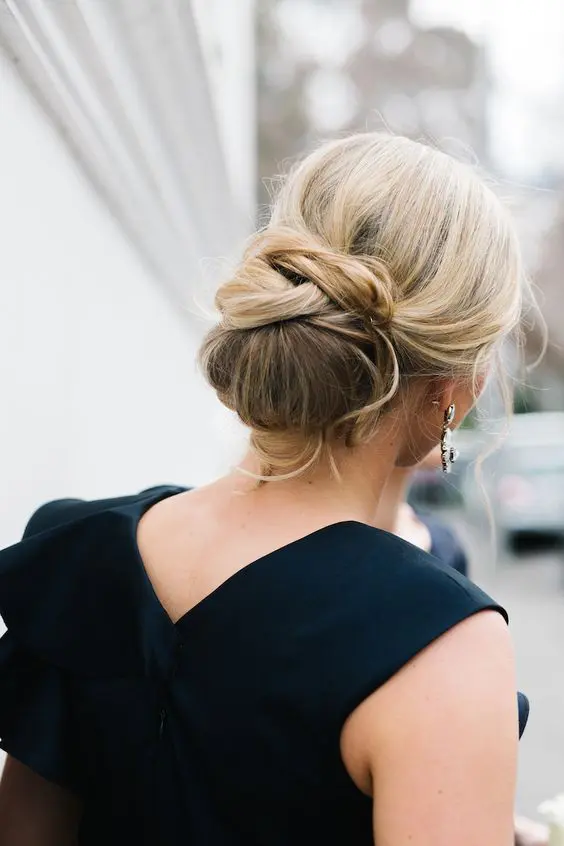 a creative low chignon hairstyle with some twists and curled bangs for a chic look