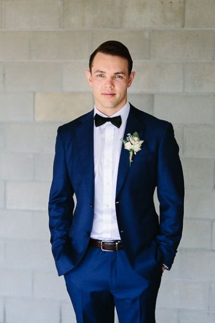 a bold blue suit with a black tow tie and a white floral boutonniere for a classic elegant look