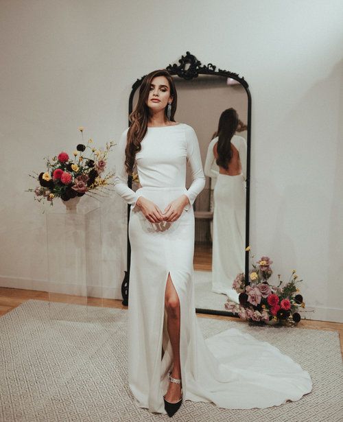 a minimalist sheath wedding dress with long sleeves, a high neckline, a front slit and a train