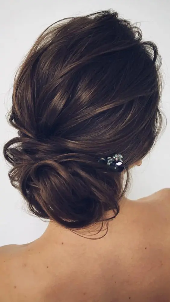 an elegant messy low updo with textures and a small rhinestone hairpiece to look effortlessly chic