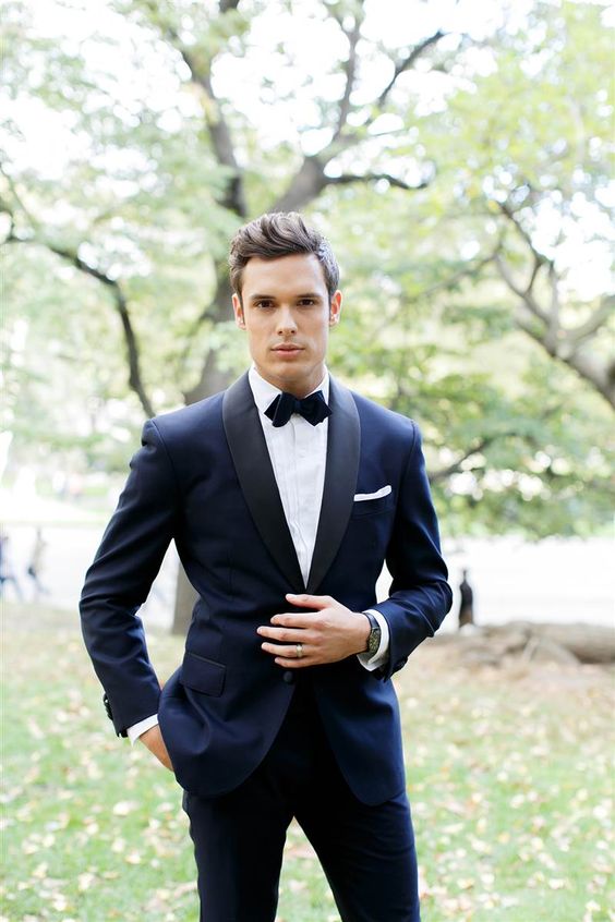 a midnight blue tuxedo with black lapels and a black velvet bow tie for a formal wedding look