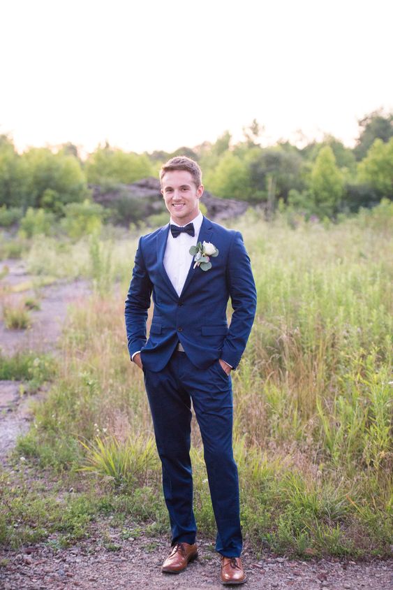 a navy blue suit, a black bow tie, brown shoes and a white rose boutonniere for a classic elegant look