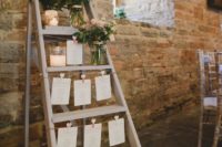 24 a seating plan made of a ladder and some sheets of paper attached to it plus blush florals in jars