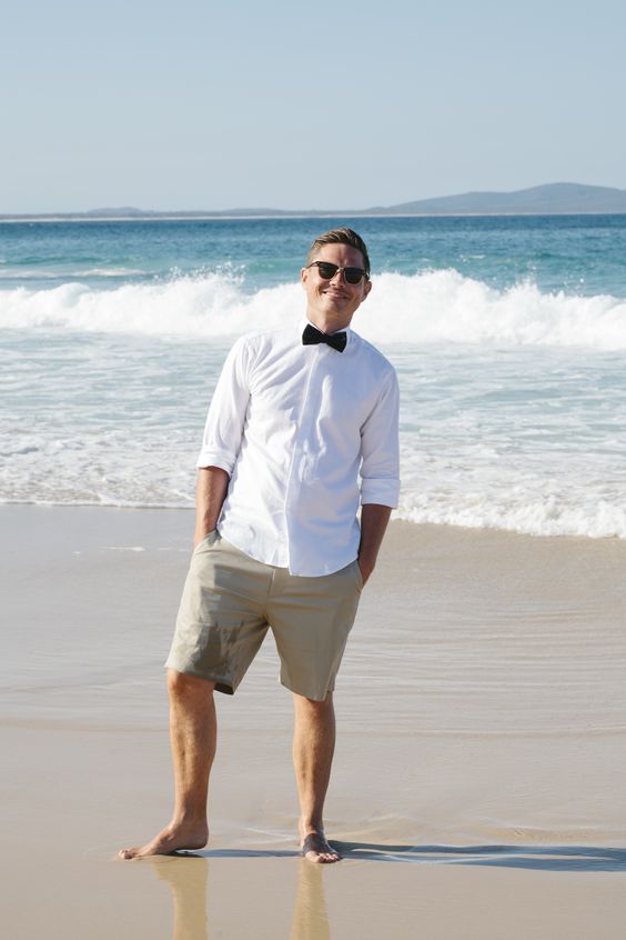 tan shorts, a white shirt with cuffed sleeves and a black bow tie for relaxed style