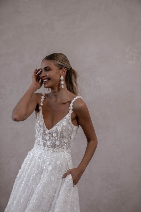 a beautiful embellished floral applique wedding dress with a V-neckline and floral straps plus pockets and statement earrings