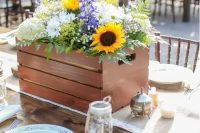 a beautiful rustic wedding centerpiece in a crate, with sunflowers, white hydrangeas, purple blooms, baby’s breath and fern is a gorgeous solution
